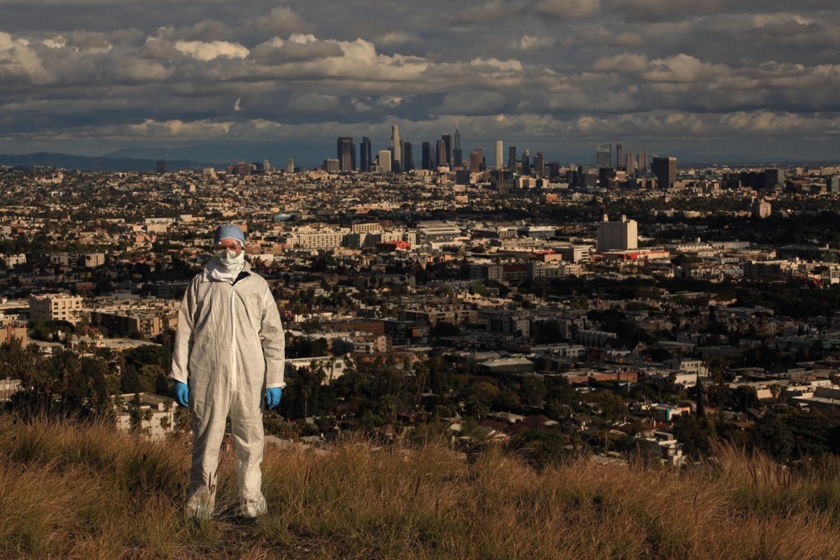 man wearing medical personal protective equipment on hill overlooking downtown Los Angeles