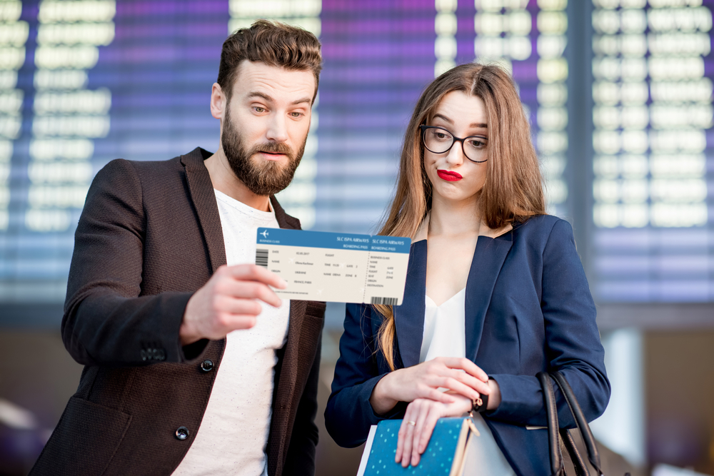 A couple looking at their flight boarding pass with a concerned look on their faces