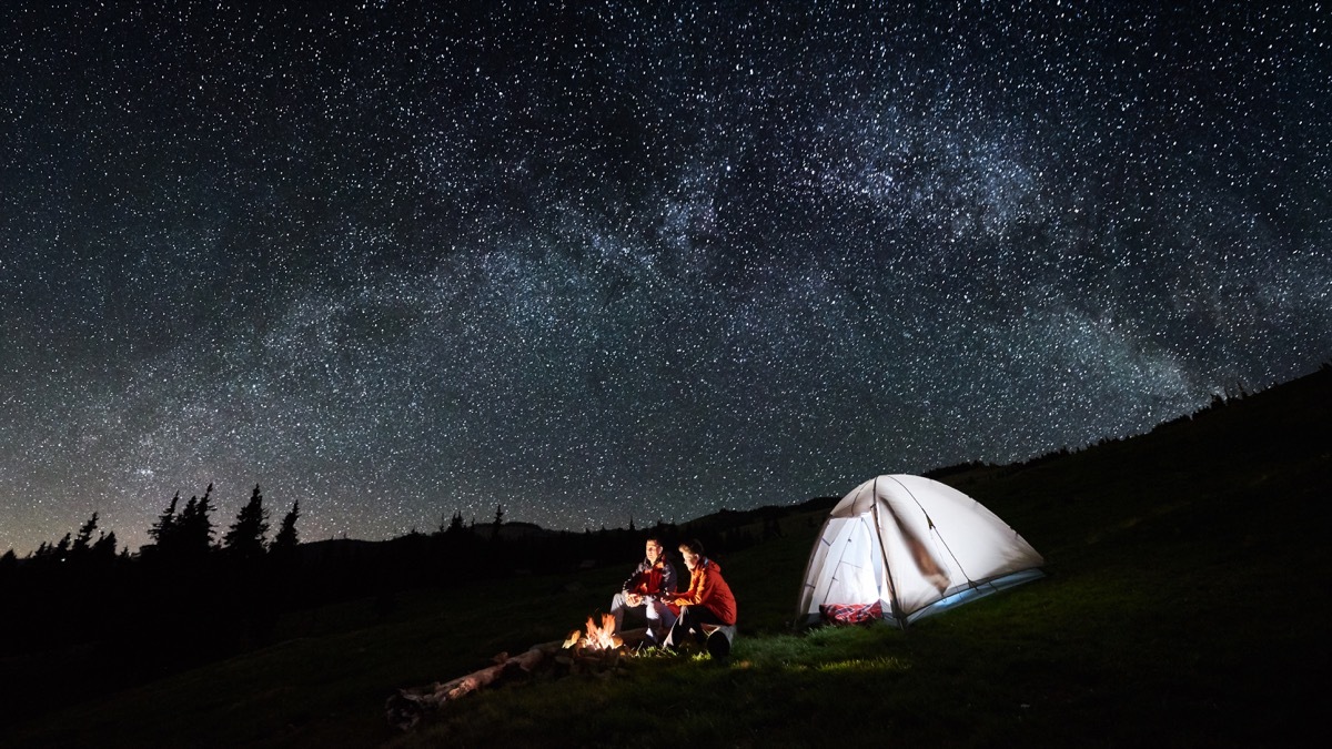 Father and son sitting by a fire camping with a tent sleeping under the stars