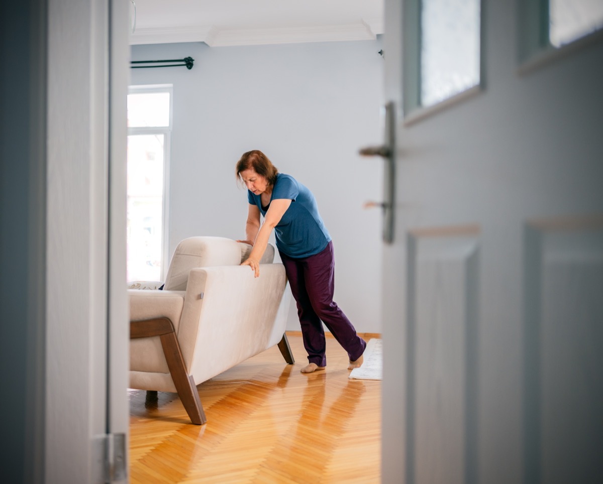 Woman suffering from dizziness with difficulty standing up while leaning on sofa