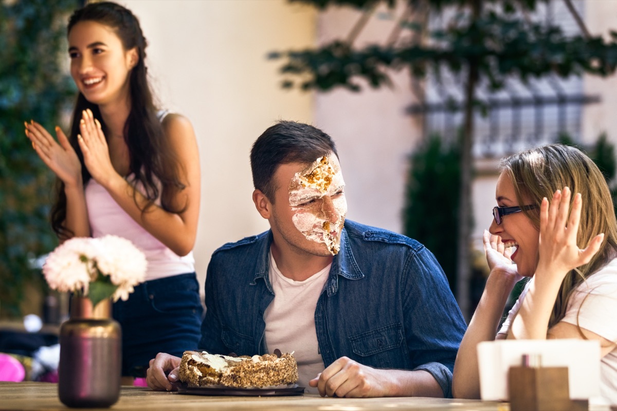 man with cake all over his face, two women laughing