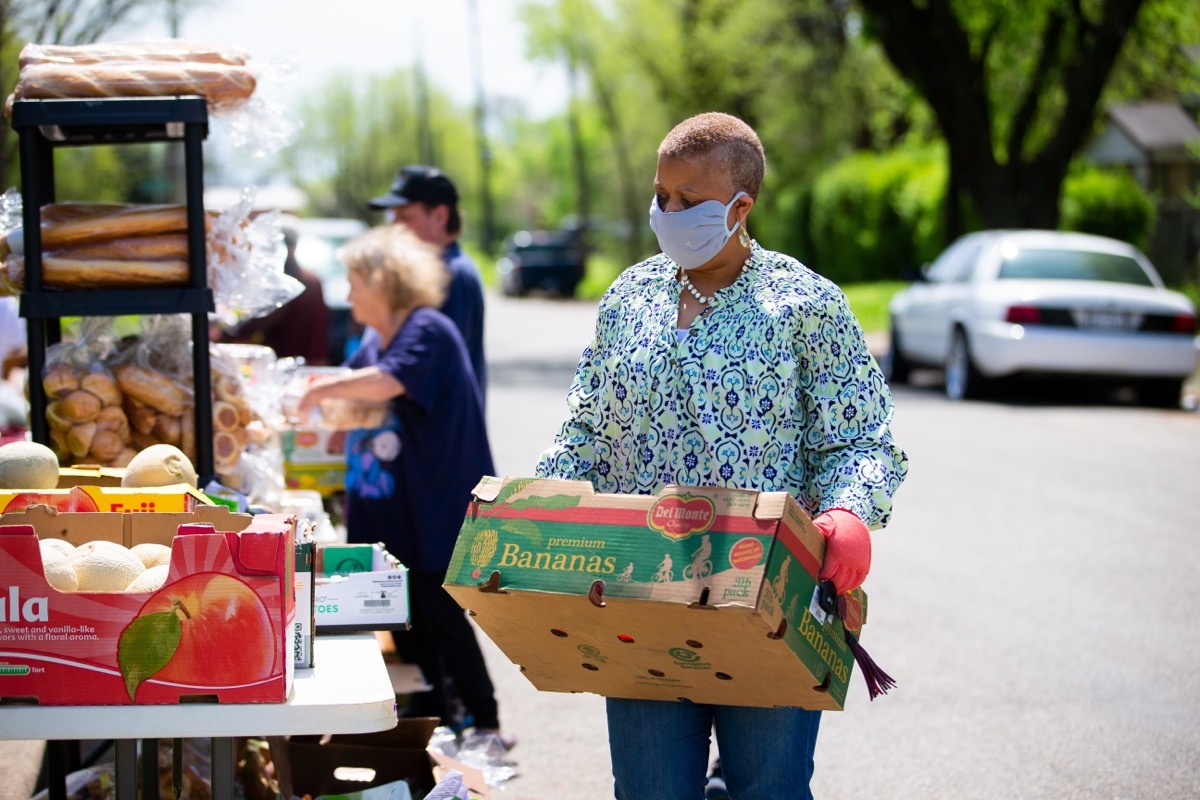 woman working at food pantry standing outdoors holding crate