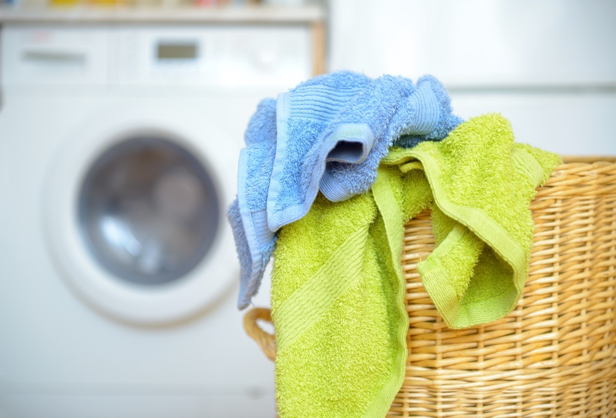 Dirty clothes basket with towels waiting for laundry with washing machine in background.