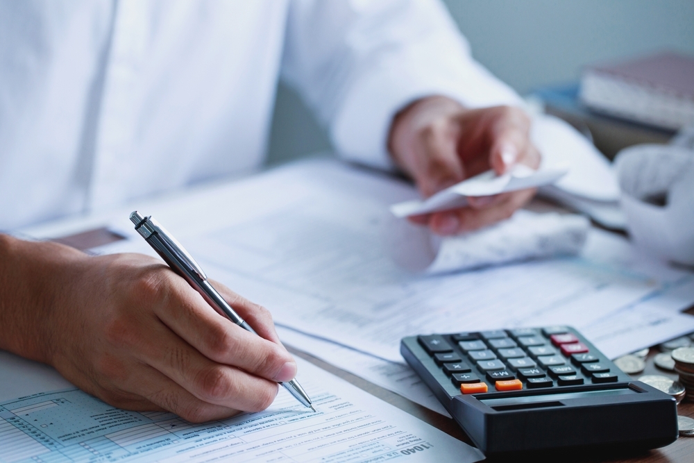 A close up of someone filling out their 1040 tax form while using a calculator