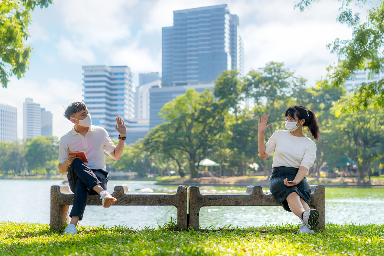 young man and woman greet and say hello to each other while wearing masks and sitting 6 feet apart