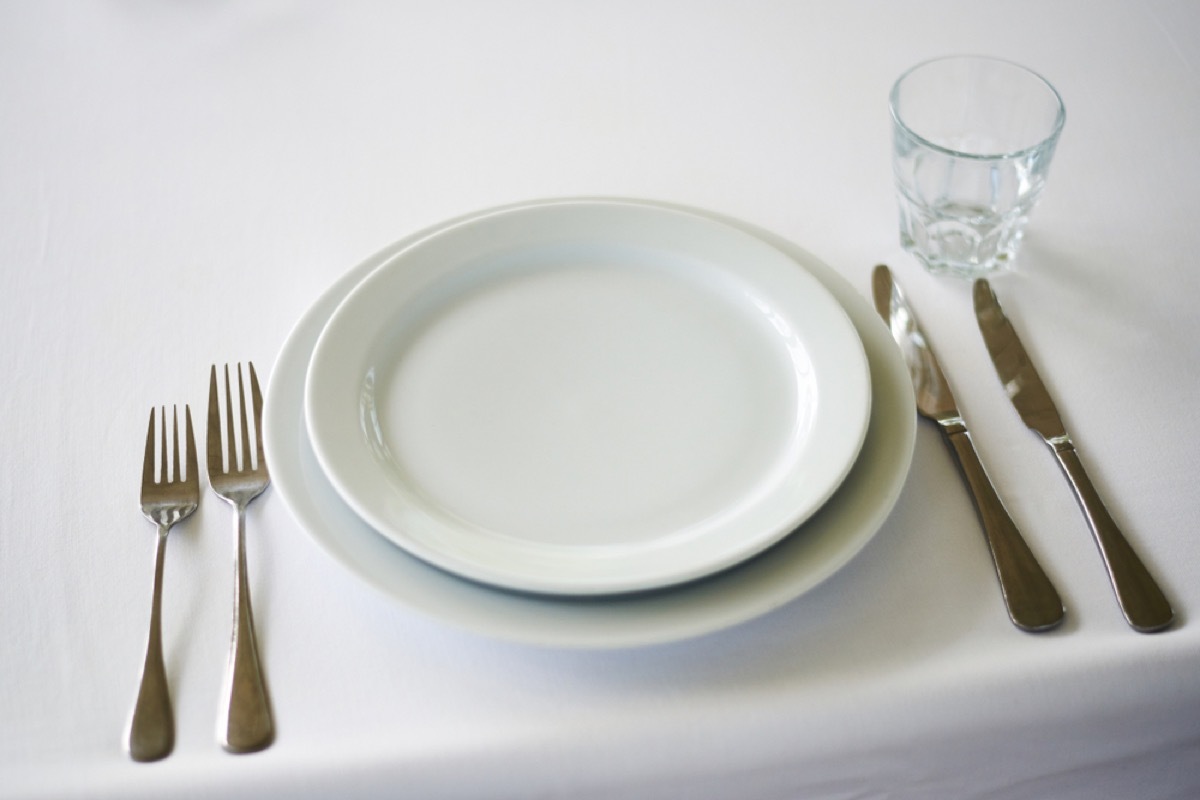 white plates and two sets of forks and knives on white tablecloth