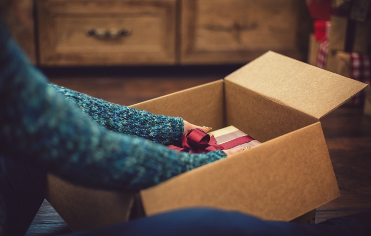 Young beautiful girl accepting and opening parcel with present box during Christmas holidays