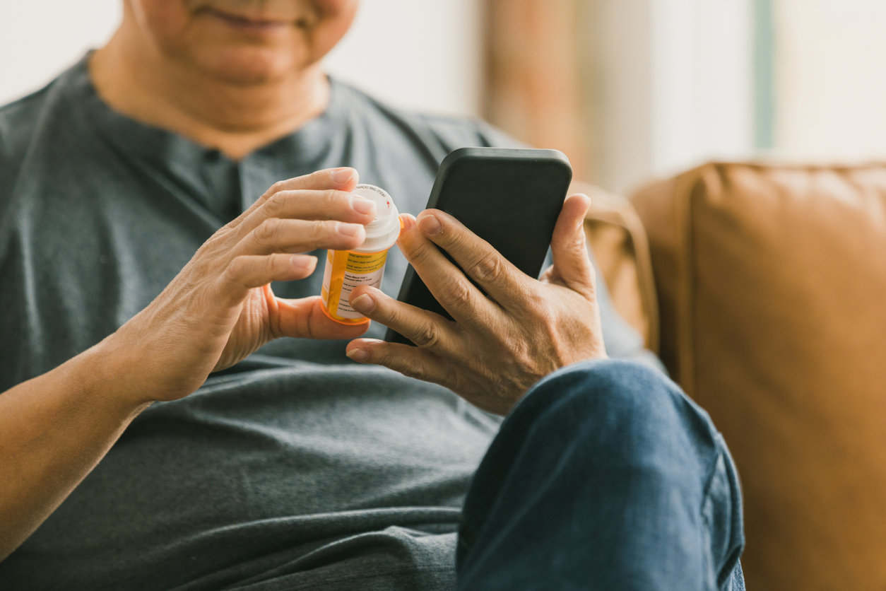 Close up of a man looking at his medication bottle while using his phone