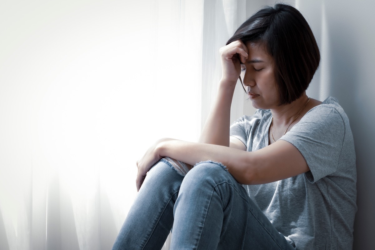 upset middle-aged asian woman sitting on floor