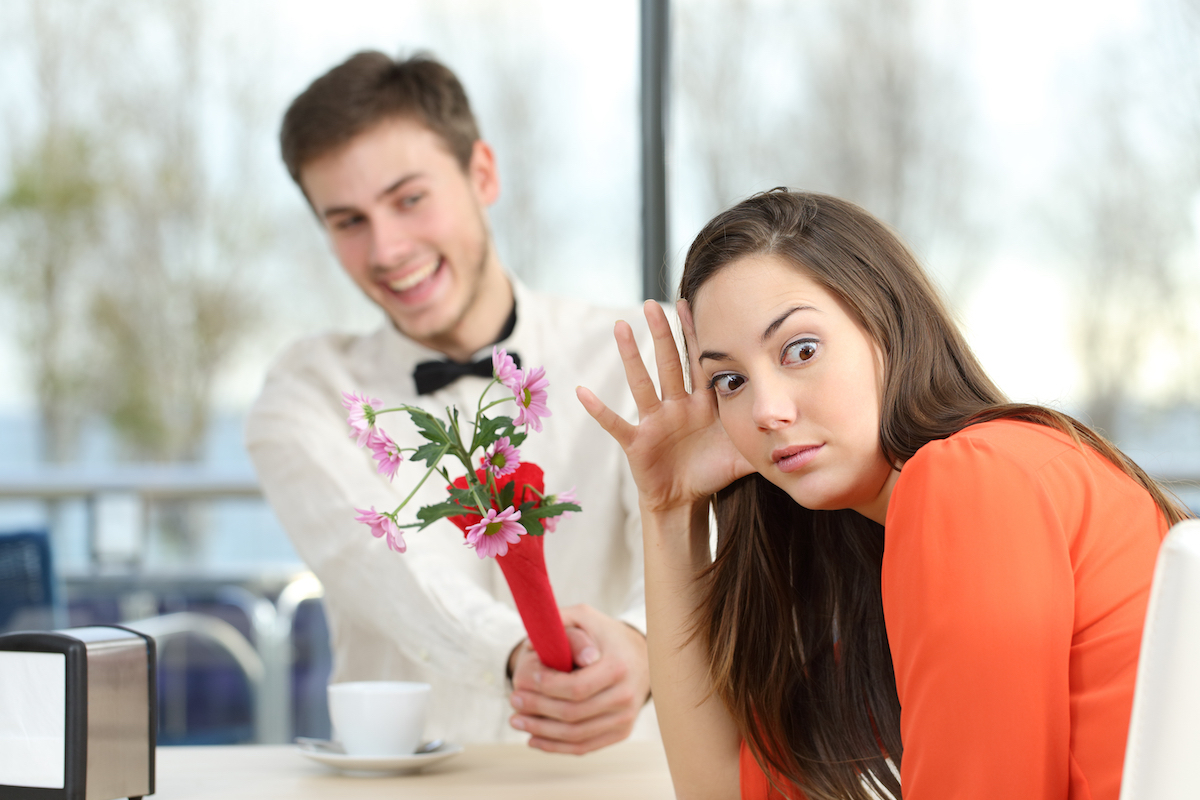 A young man shoving flowers at his date while she rolls her eyes.