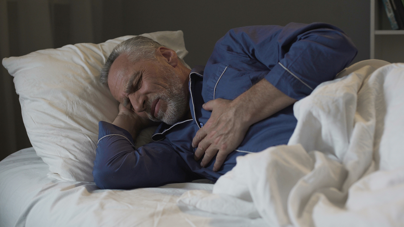 A senior sleeping while holding his heart in discomfort