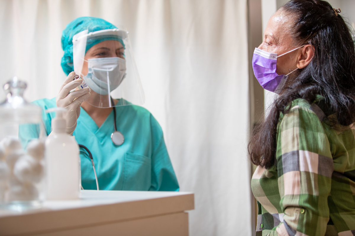 Senior woman wearing protective face mask sitting in doctor's office and waiting for COVID vaccination