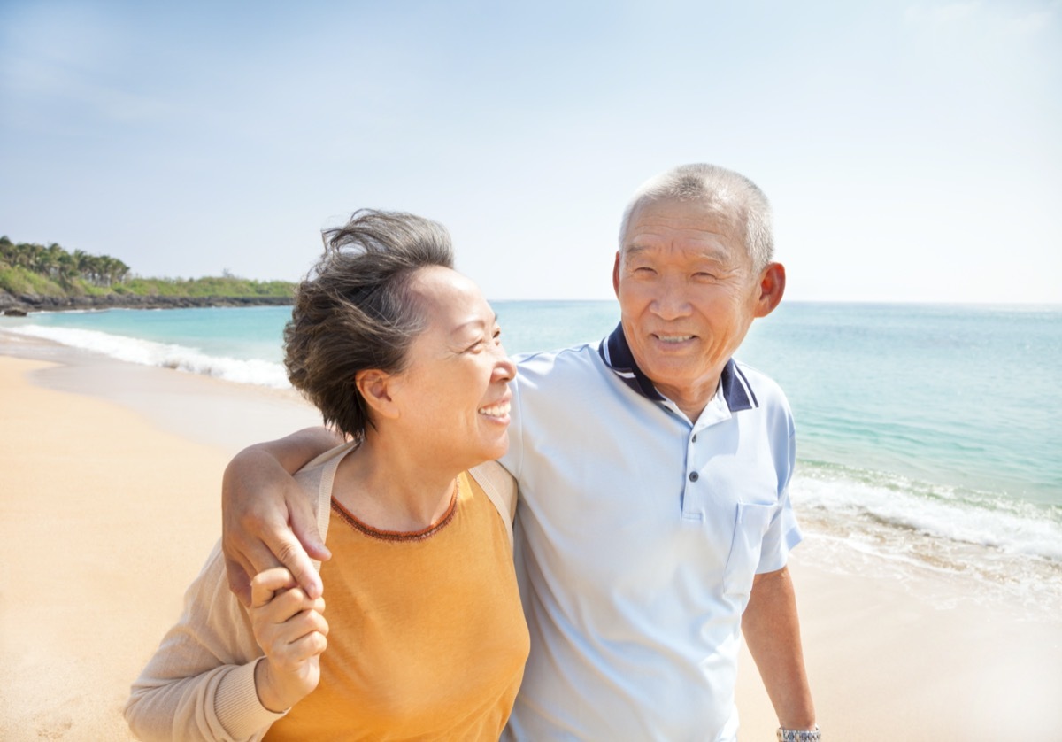 older asian couple walking on beach