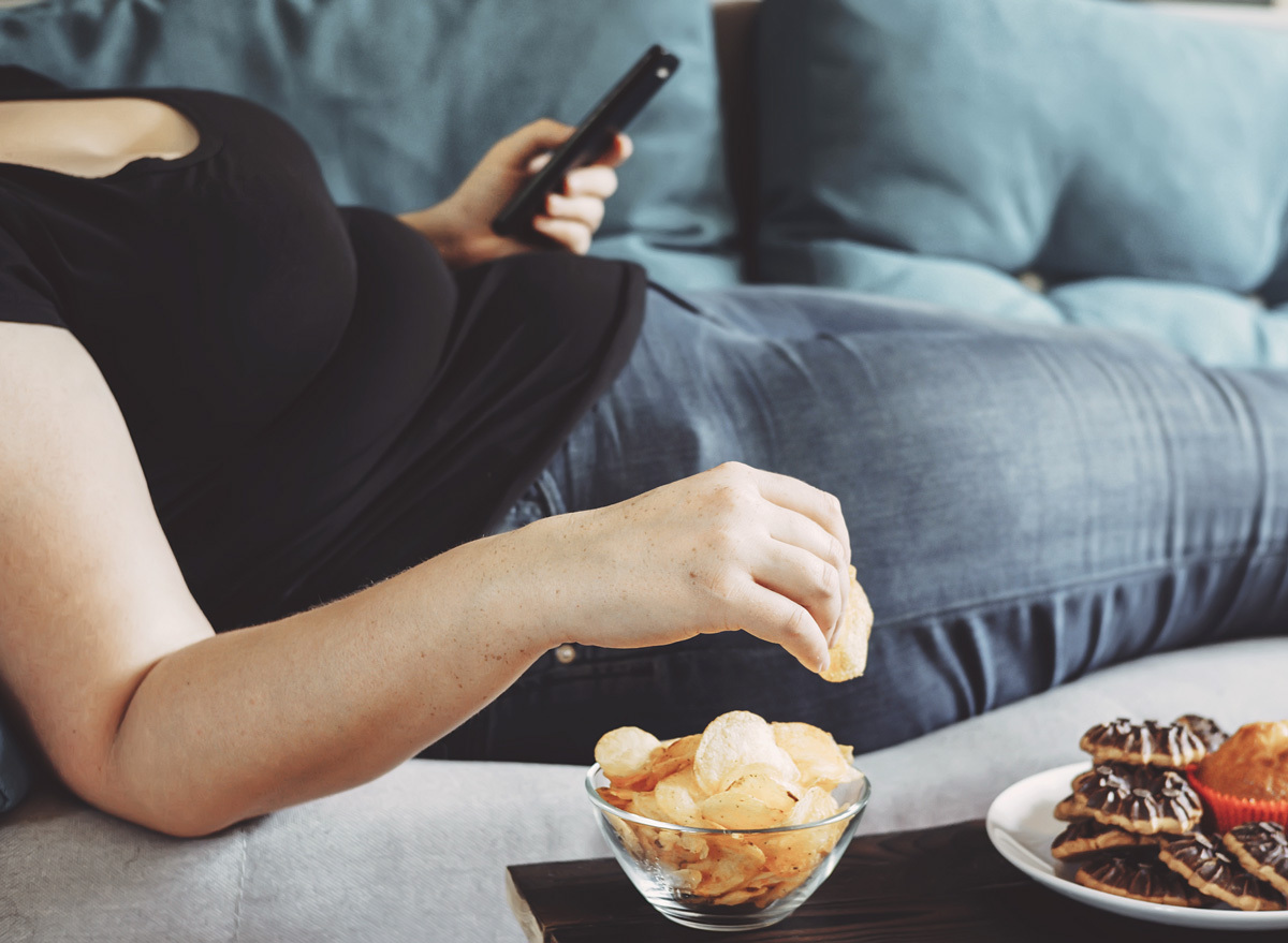 Woman emotional eating chips on couch scrolling through phone