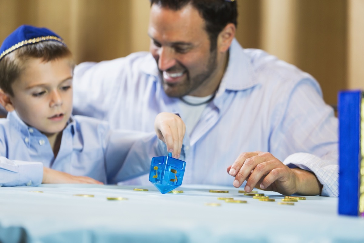 man and young son in yarmulke playing dreidel