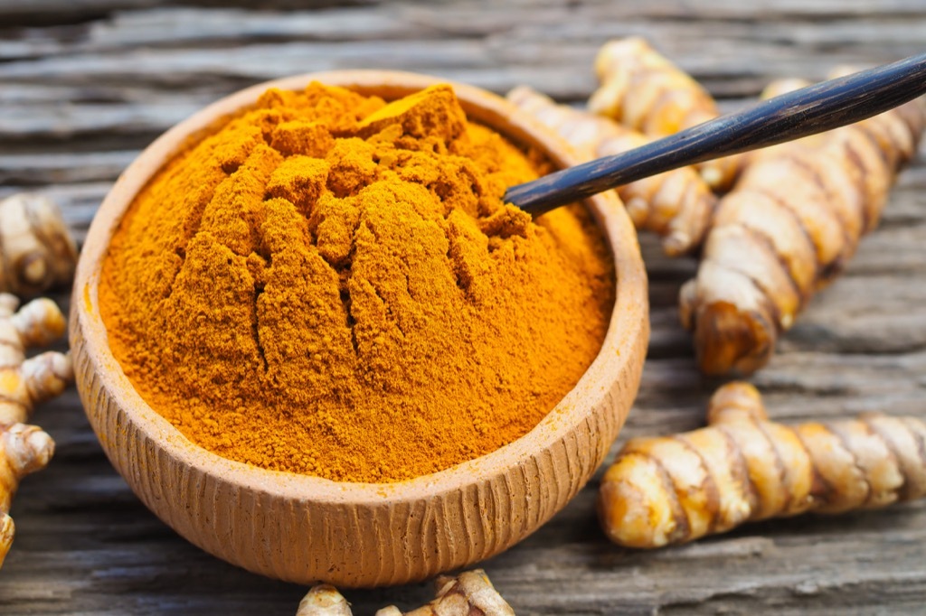 turmeric curcumin powder in a bowl with turmeric pieces in the background