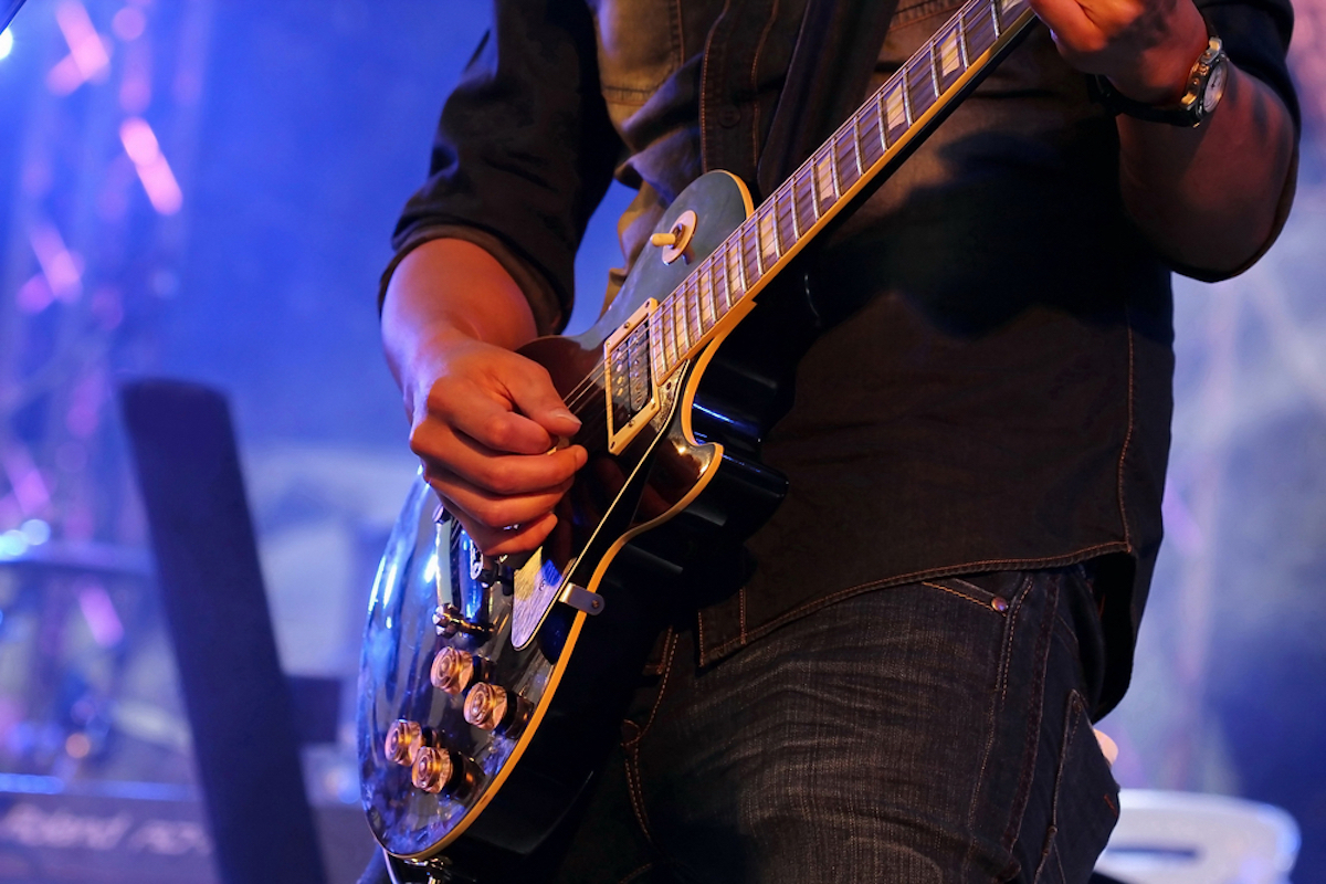  Guitarist's hand playing electric guitar on concert stage with blue light