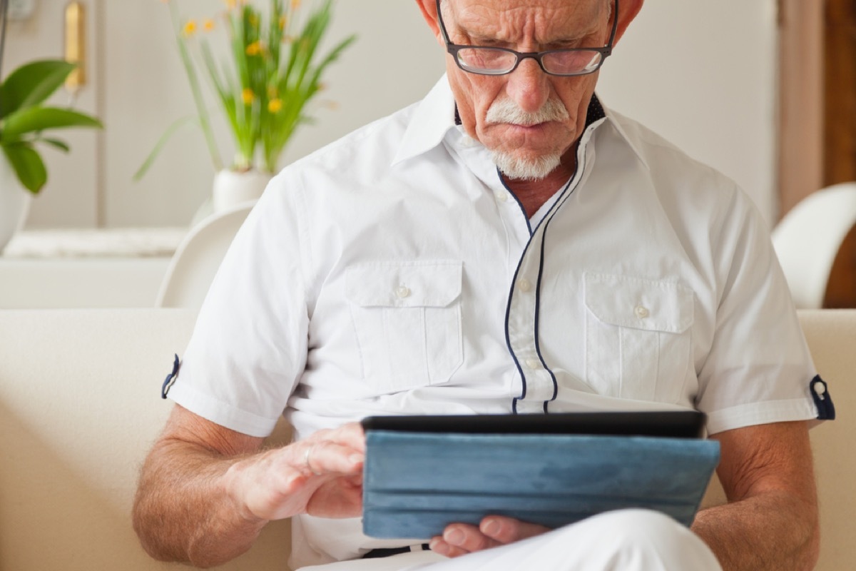 older white man using his tablet on couch