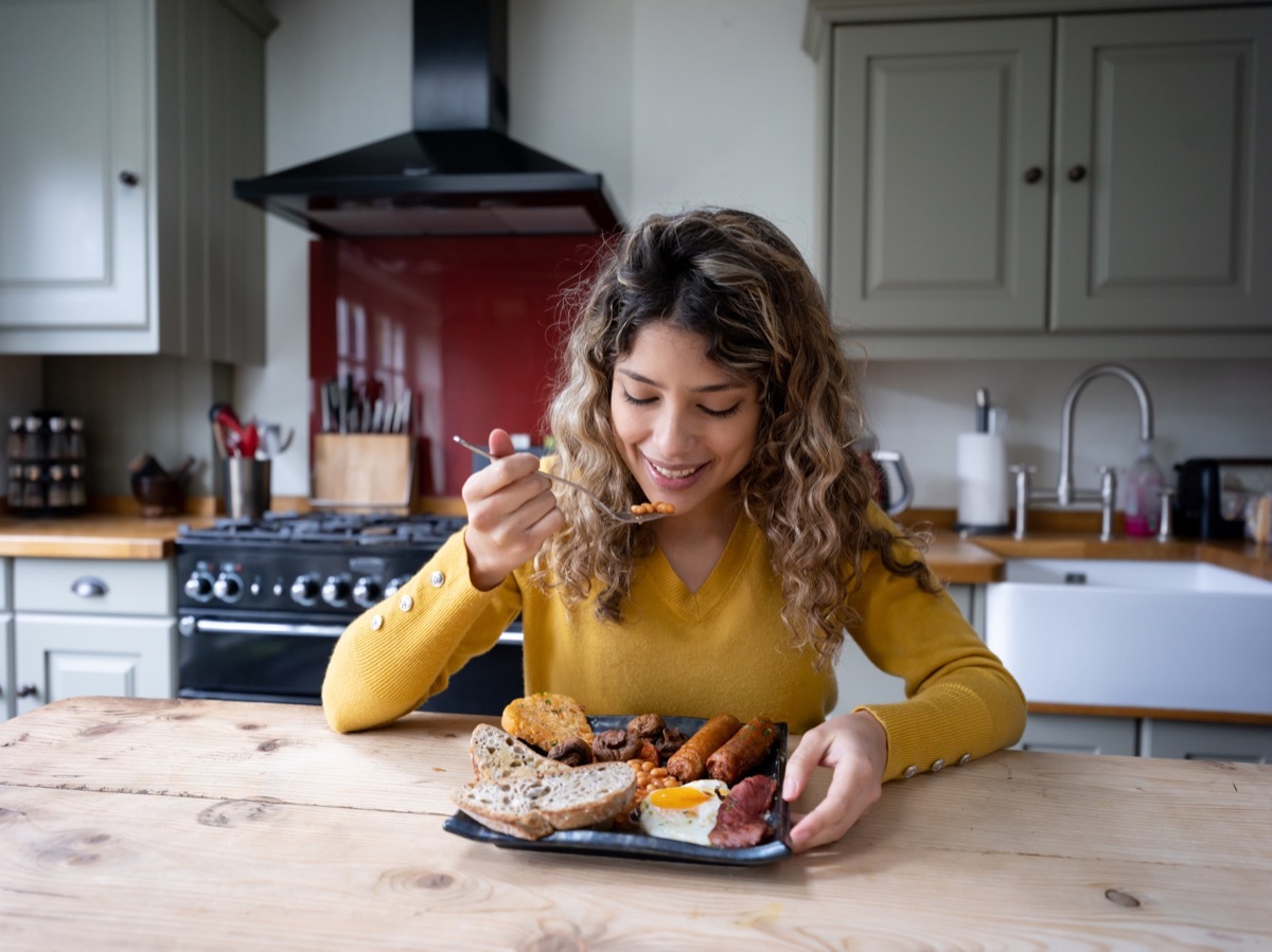 Beautiful young woman at home enjoying a delicious english breakfast