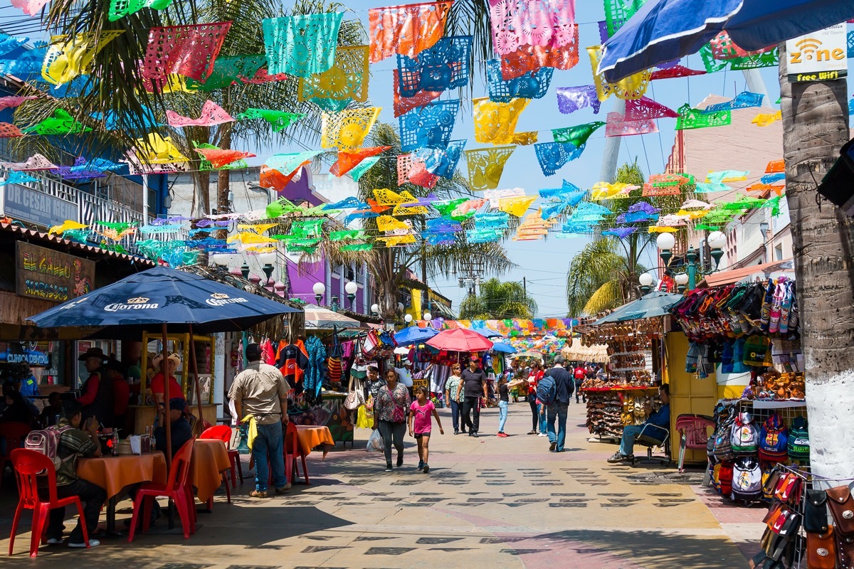 colorful flags hang over a pedestrian street with sidewalk tables in tijuana