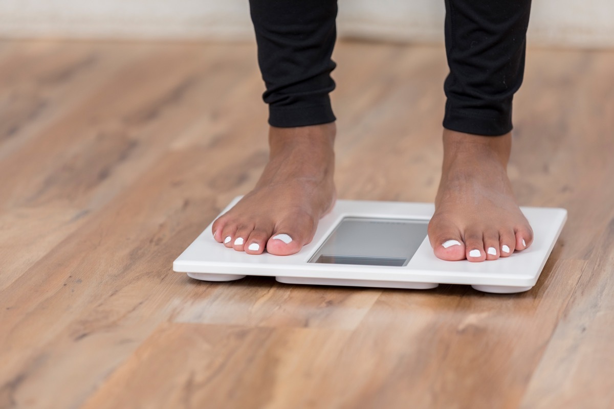 Woman weighing herself on a scale for potential weight loss or weight gain