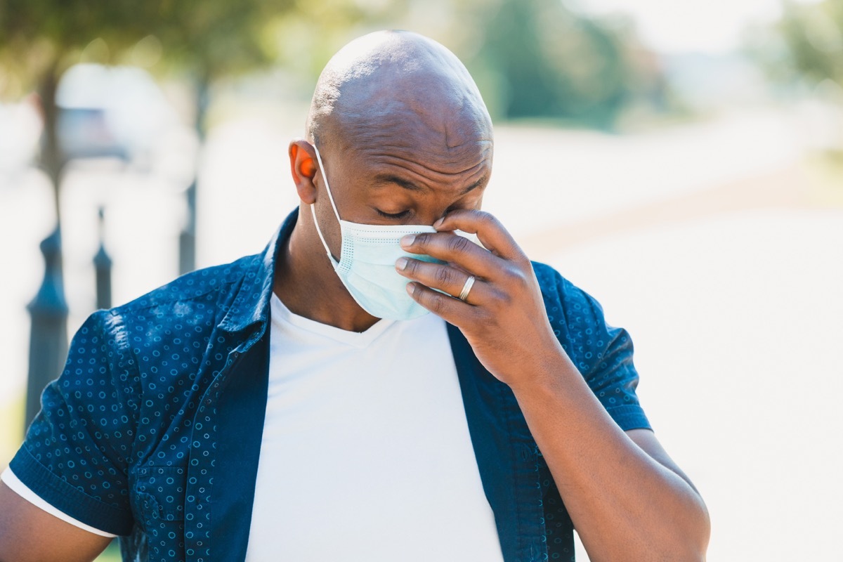 A tired man adjusts his face mask while outdoors during the COVID-19 crises.