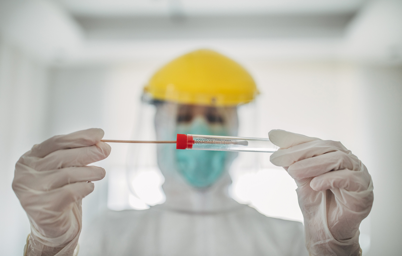 female doctor in protective suit holding and showing covid-19 tube test and sampling swab.