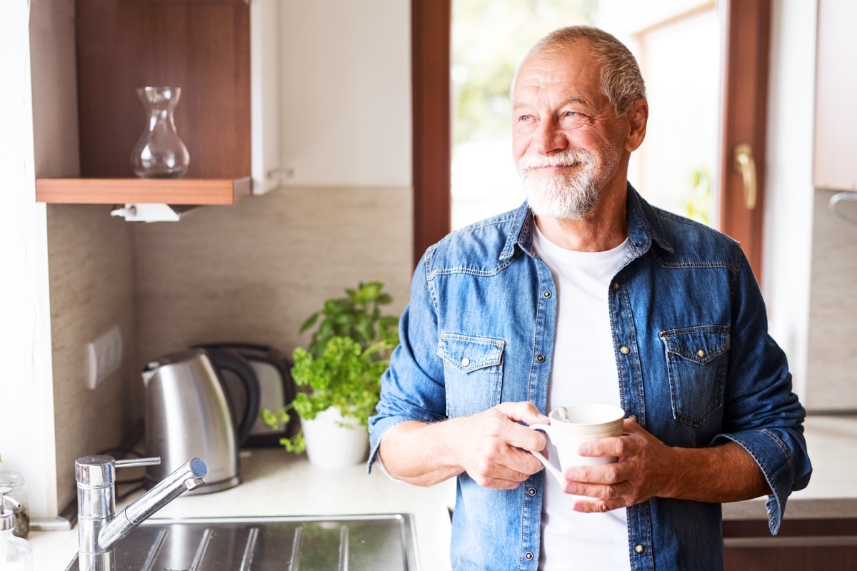 Older man in kitchen drinking coffee smiling