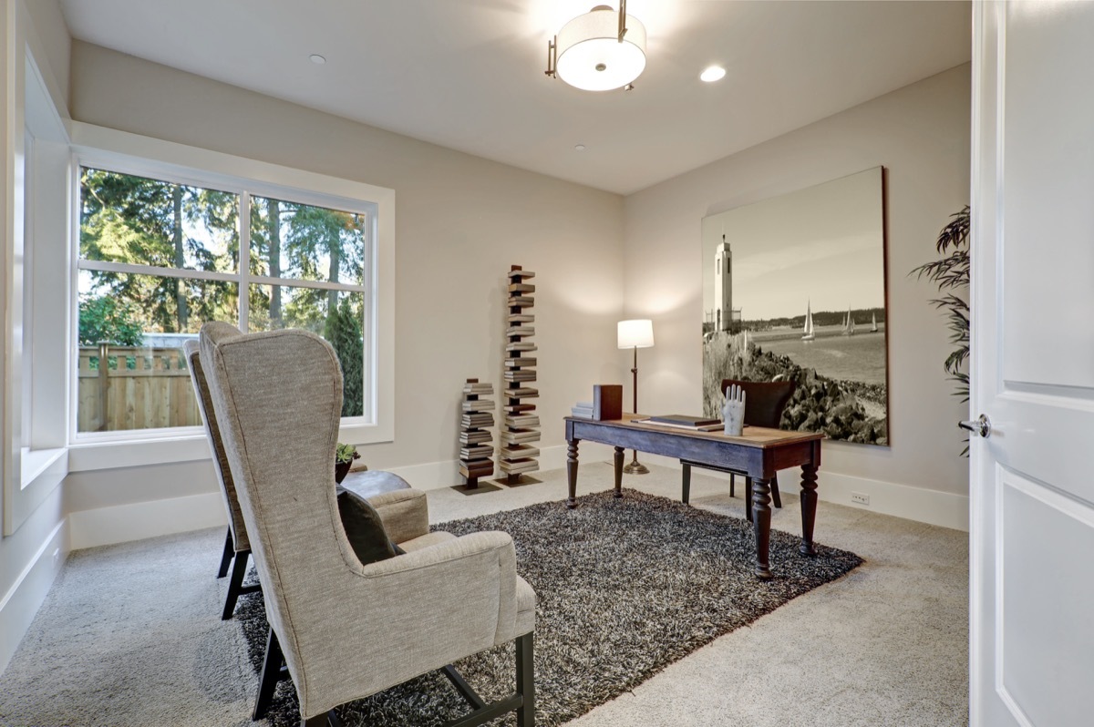 Brown and beige office design boasts dark wood table with turned legs facing linen wingback chairs atop fluffy gray rug. Northwest, USA