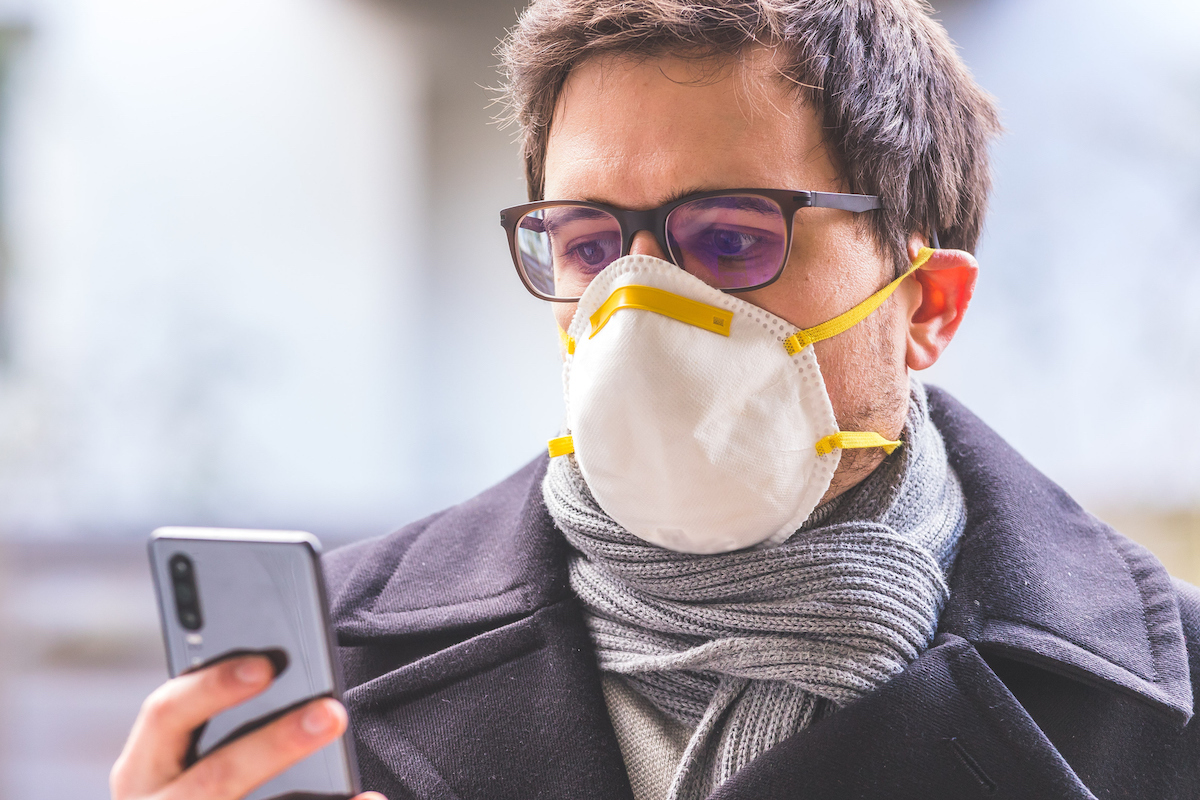 Man outdoors with a mask and smartphone reading about COVID