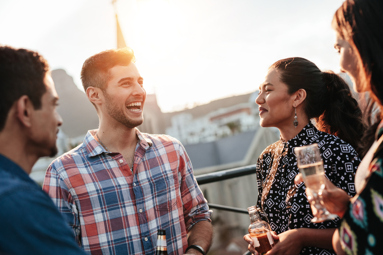 Happy young man chatting and laughing with friends. Young people having a good time together during rooftop party.