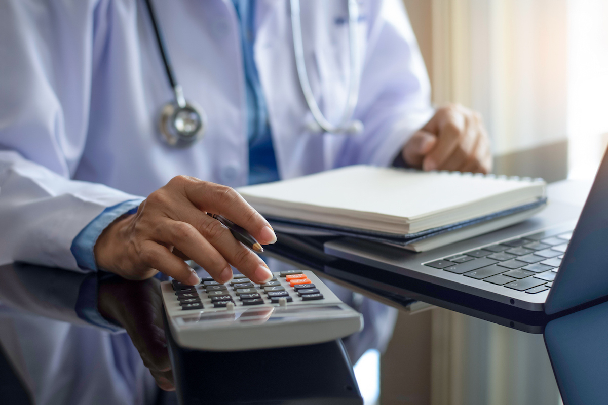 Doctor with stethoscope using calculator and work on computer notebook on the desk at modern office at clinic or hospital. 