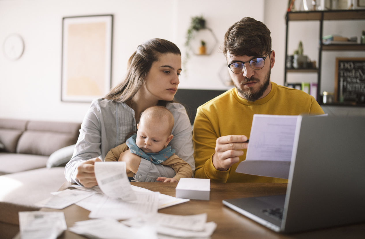 A young family sitting down at the kitchen table to pay taxes or bills on their laptop