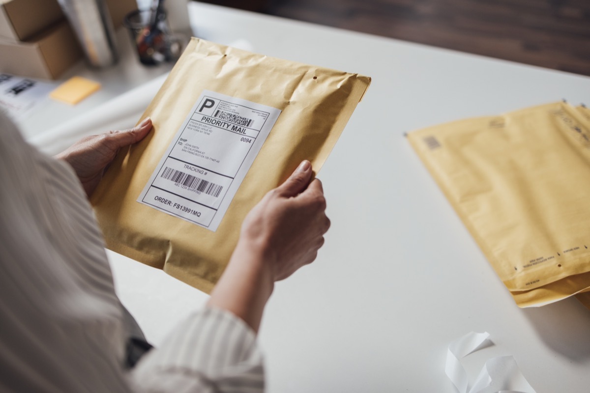 Hands of an unrecognisable small business owner holding a yellow envelope with shipping details before dispatching it