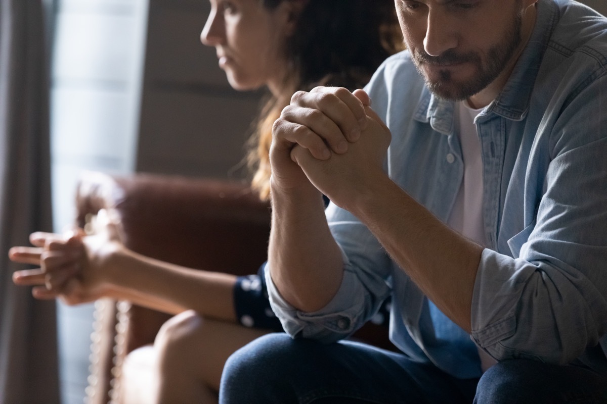 young couple sitting on couch looking unhappy due to argument over infidelity or cheating