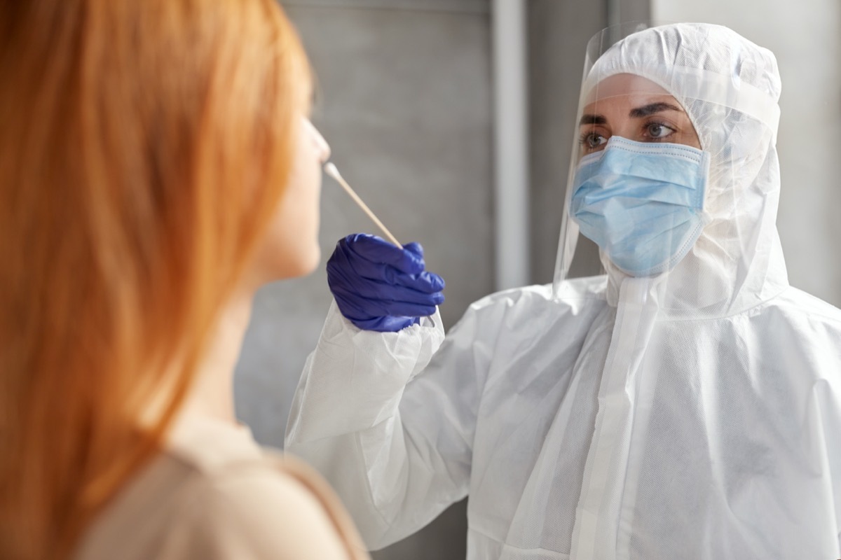 doctor or healthcare worker in protective wear, medical mask and face shield making coronavirus test and taking sample from patient