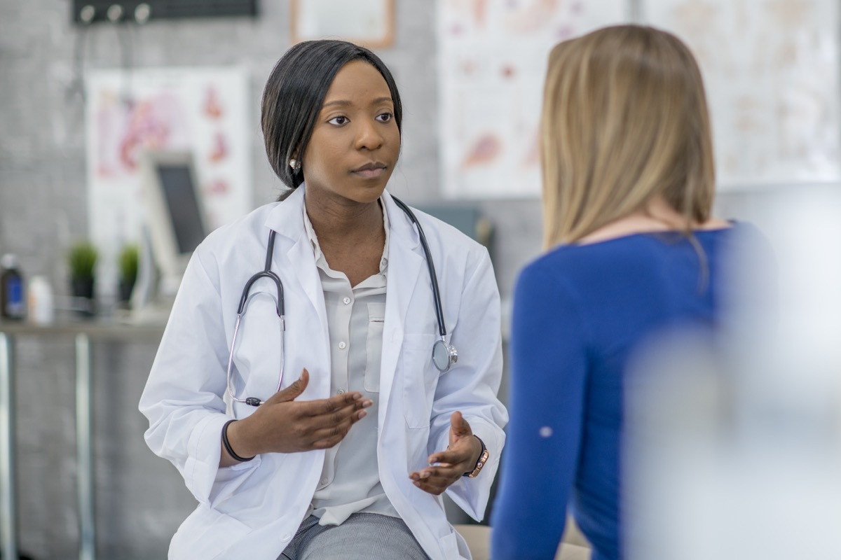 woman in blue shirt photographed from behind talking to a young doctor with a stethoscope around her neck