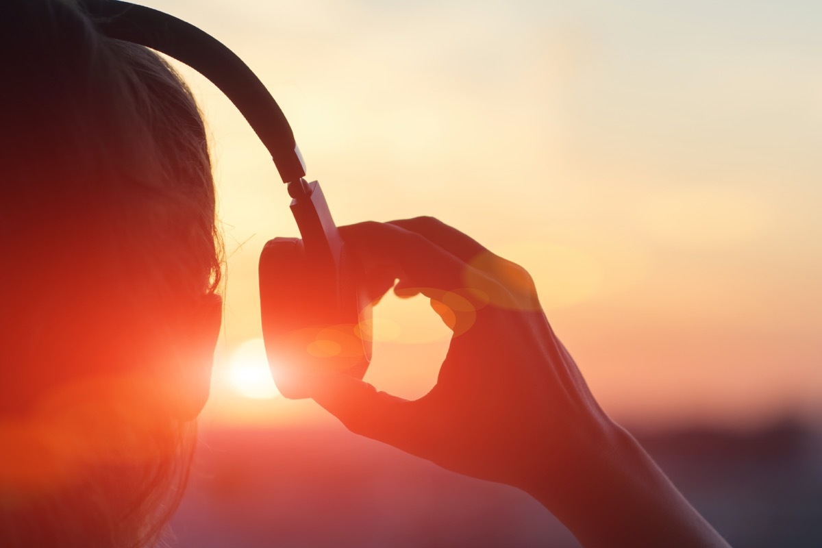 woman putting on over-ear headphones at sunset - sound facts