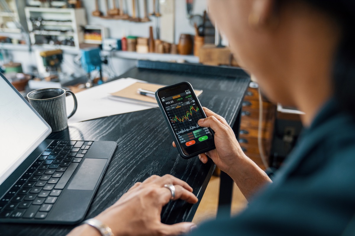 Mid adult man using a smart phone to monitor his cryptocurrency and stock trading. He is in his small jewellery workshop.