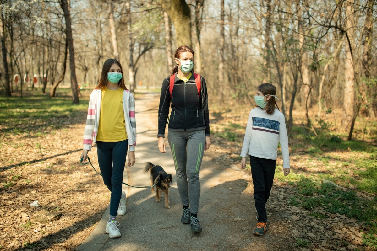 mother and two daughters in face masks walking their dog in a park