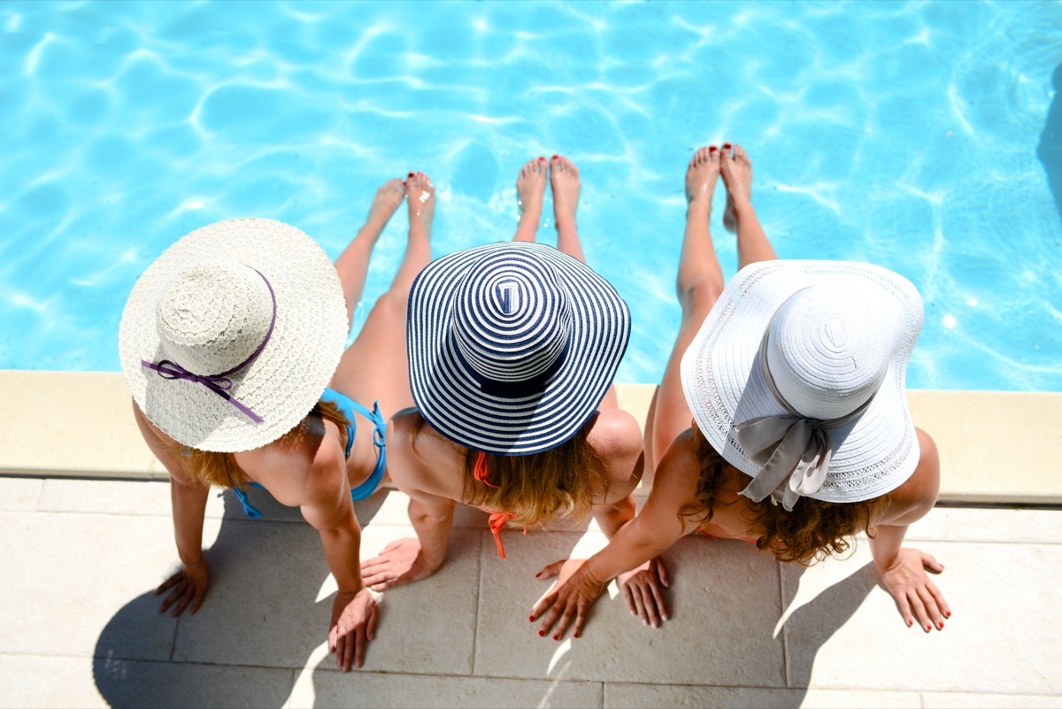 Three women wearing sun hat sitting by the poolside of a resort swimming pool during summer holiday.