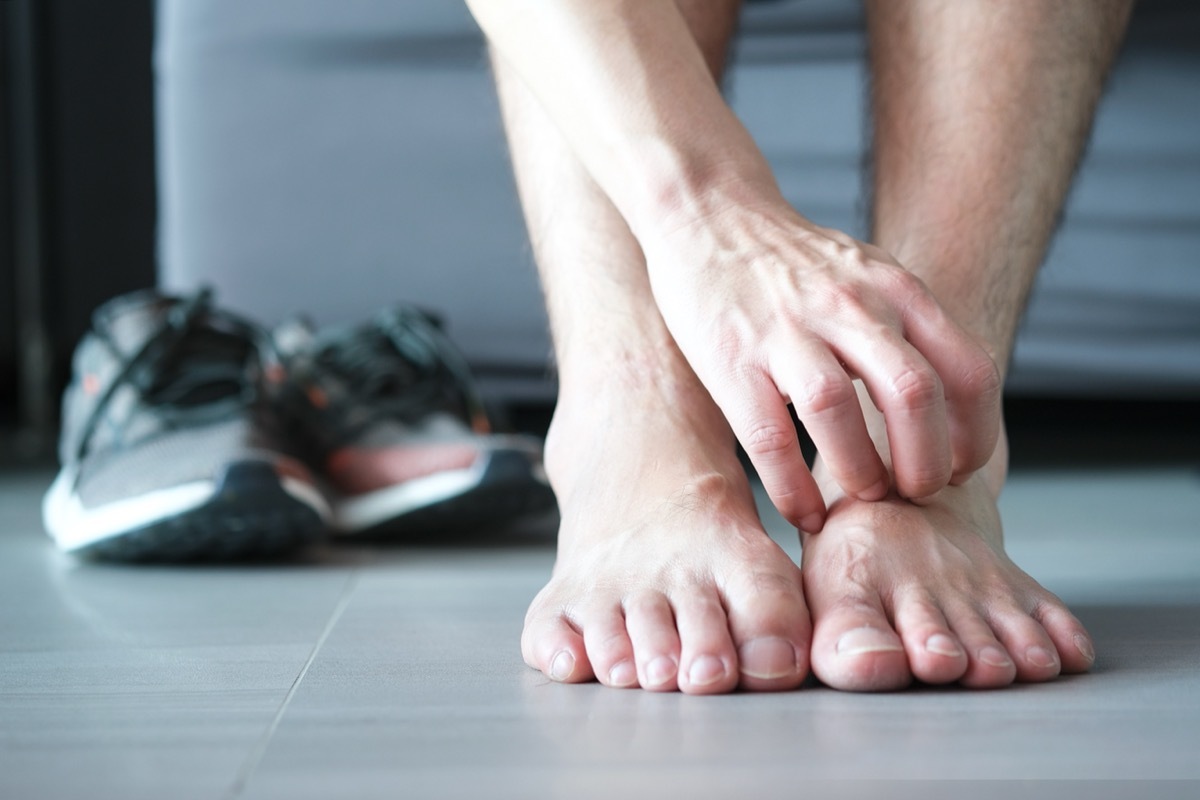 man scratching foot with gray sneakers in the background