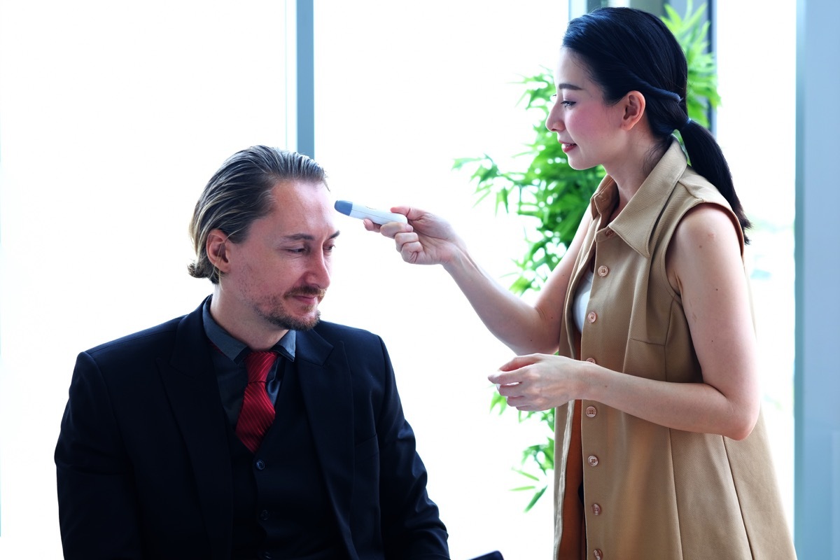 young asian woman giving white male employee temperature check for coronavirus