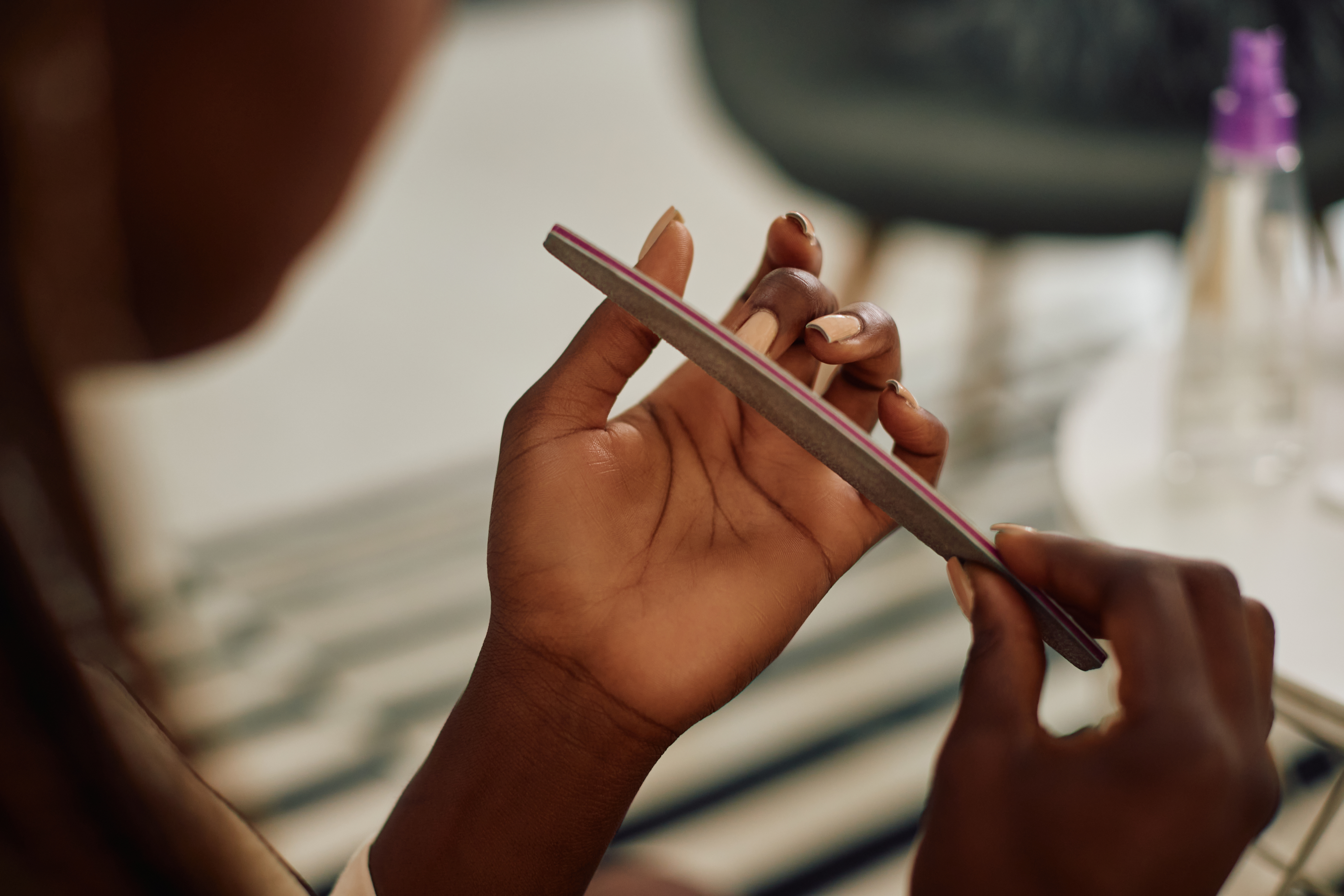 Close-up of African American woman using nail file while polishing her nails at home.