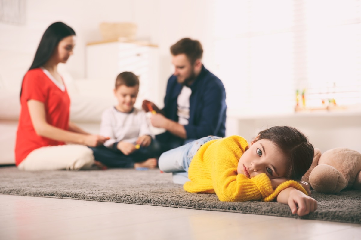 Unhappy little girl feeling jealous while parents spend time with her brother at home