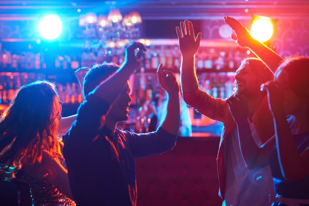 young people dancing inside bar with red and blue lights