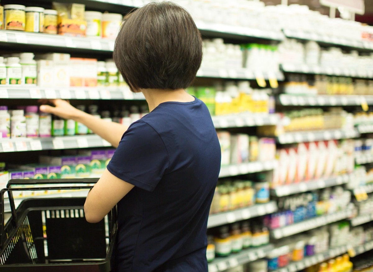 Woman Shopping at Grocery Market Pharmacy. Supermarket Shopper Doing Groceries. Female Holding Basket Trying to Decide which Products to Buy. Retail Healthcare Medicine, Vitamins, and Supplements.