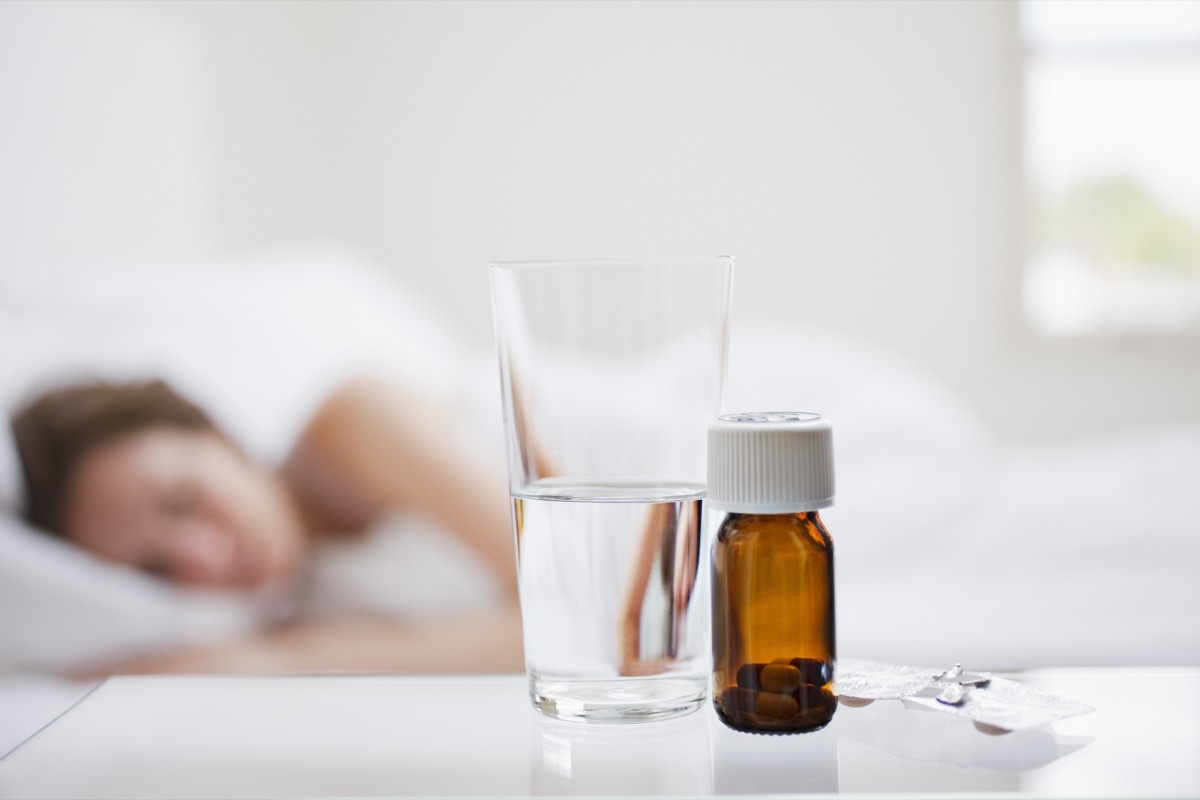 Close up of pill bottle with sick woman in background