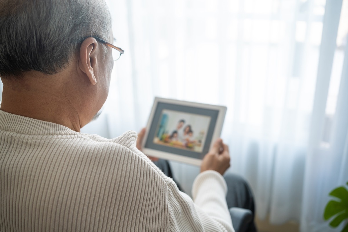 senior male sit alone on wheelchair and looks family photographs. Elderly older mature grandfather feel lonely and sad, missing his relative and wife while stay in nursing home after retirement.