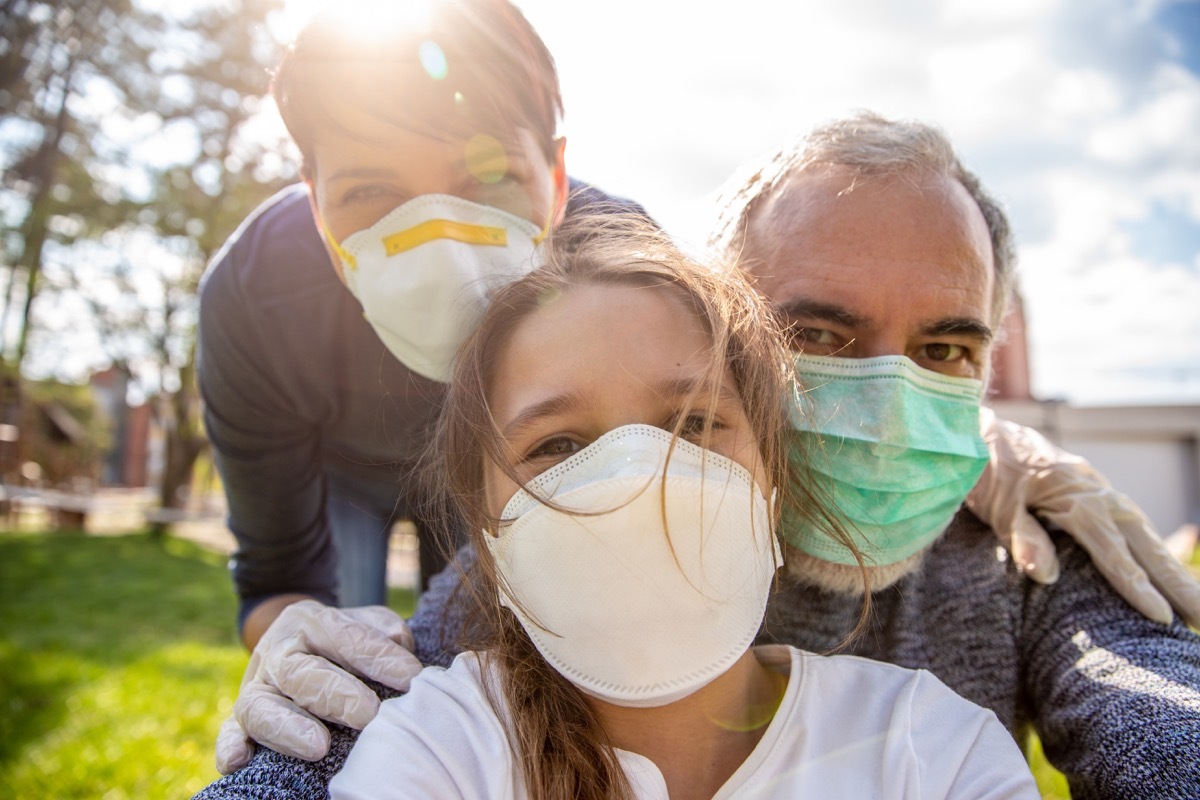 A girl taking a selfie of her family outdoors with face masks.